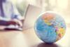 A globe map on a table in front of a man working on a laptop