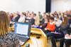 A speaker with a laptop presents to a conference audience