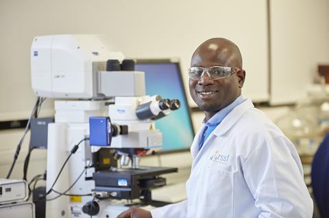 A man in an RSSL lab coat operates an optical microscope