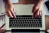 An image showing a man's hands typing on a laptop keyboard