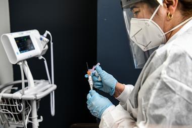 An image showing a nurse in PPE holding a syringe holding with a Covid-19 vaccine