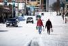 A photo of two people walking along a snow covered city road, carrying shopping bags