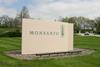 An image of an upright white stone slab displaying the word Monsanto, set on a bright green lawn