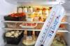 A close-up photo of a plastic fridge thermometer that shows a temperature close to 0C. In the background, an open fridge shows shelves filled with food.