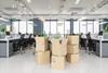 A photo of a well-lit open-plan office space. There are a few stacks of moving boxes piled in front of one of the desk rows.