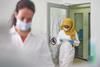 A woman wearing a headscarf and lab coat entering a laboratory through a door while reading a tablet