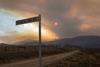 A road sign for Bumbalong Road by a track through the Australian outback in the distance heavy smoke from wildfires obscures the sun