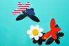 Two butterflies made of paper, one with an American flag on its wings the other with the Chinese flag, approach a paper flower.